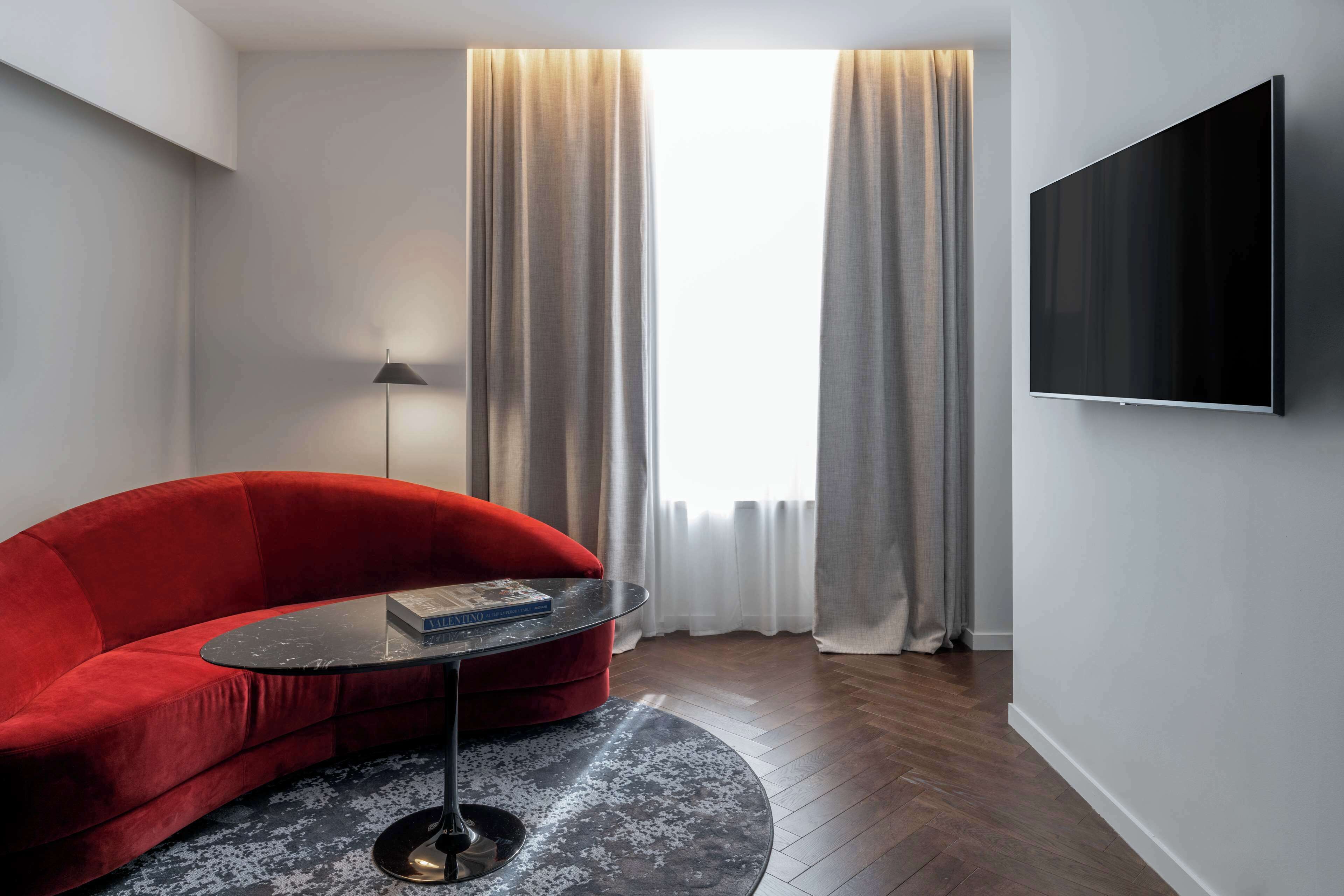 Un salon moderne avec un canapé rouge, une table basse ronde, un lampadaire et un téléviseur fixé au mur.