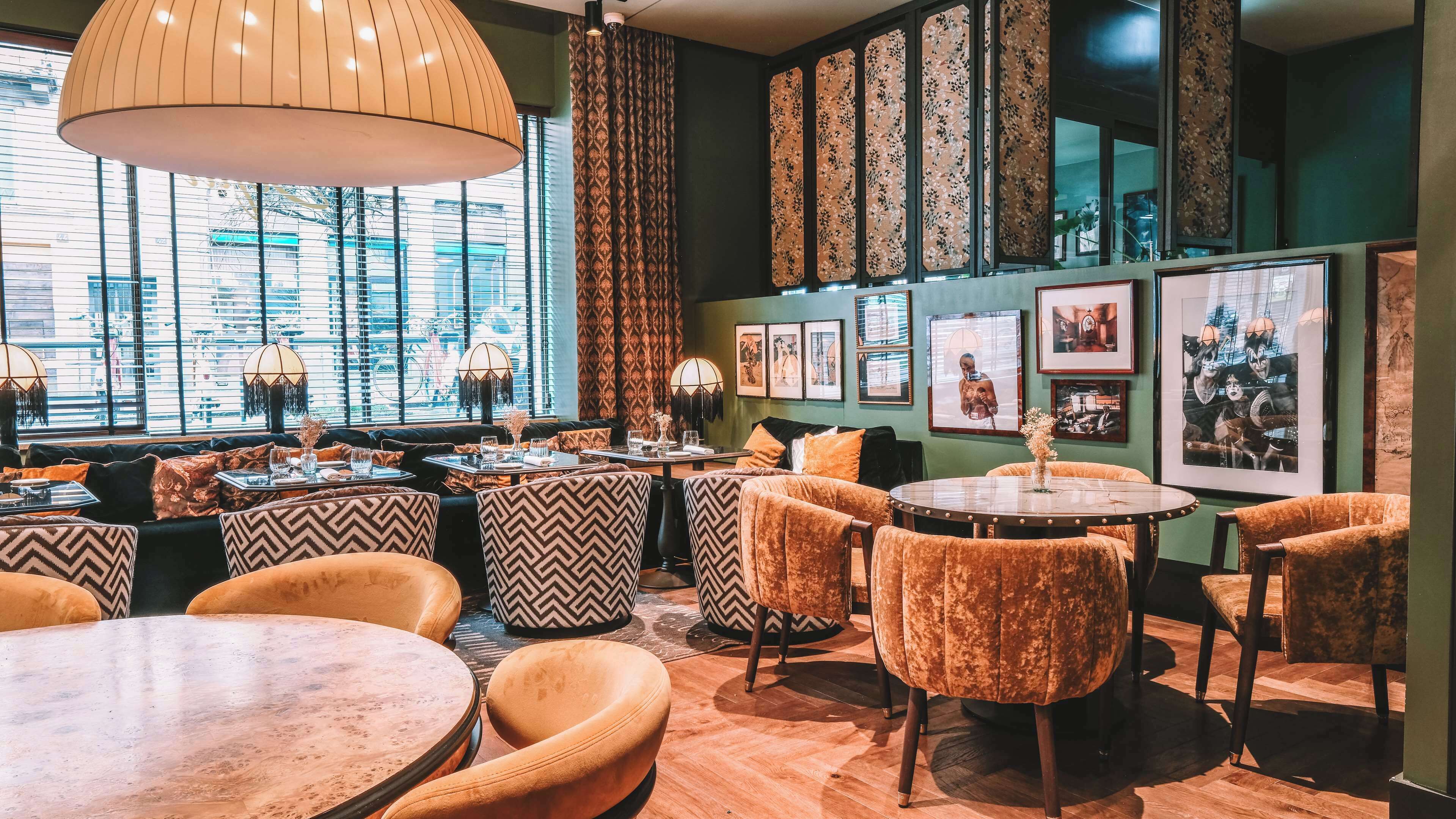 Ein gemütliches Restaurant mit einer Mischung aus moderner und klassischer Einrichtung, mit gemusterten Kissen, verschiedenen Sitzmöglichkeiten und Kunstwerken an den Wänden.