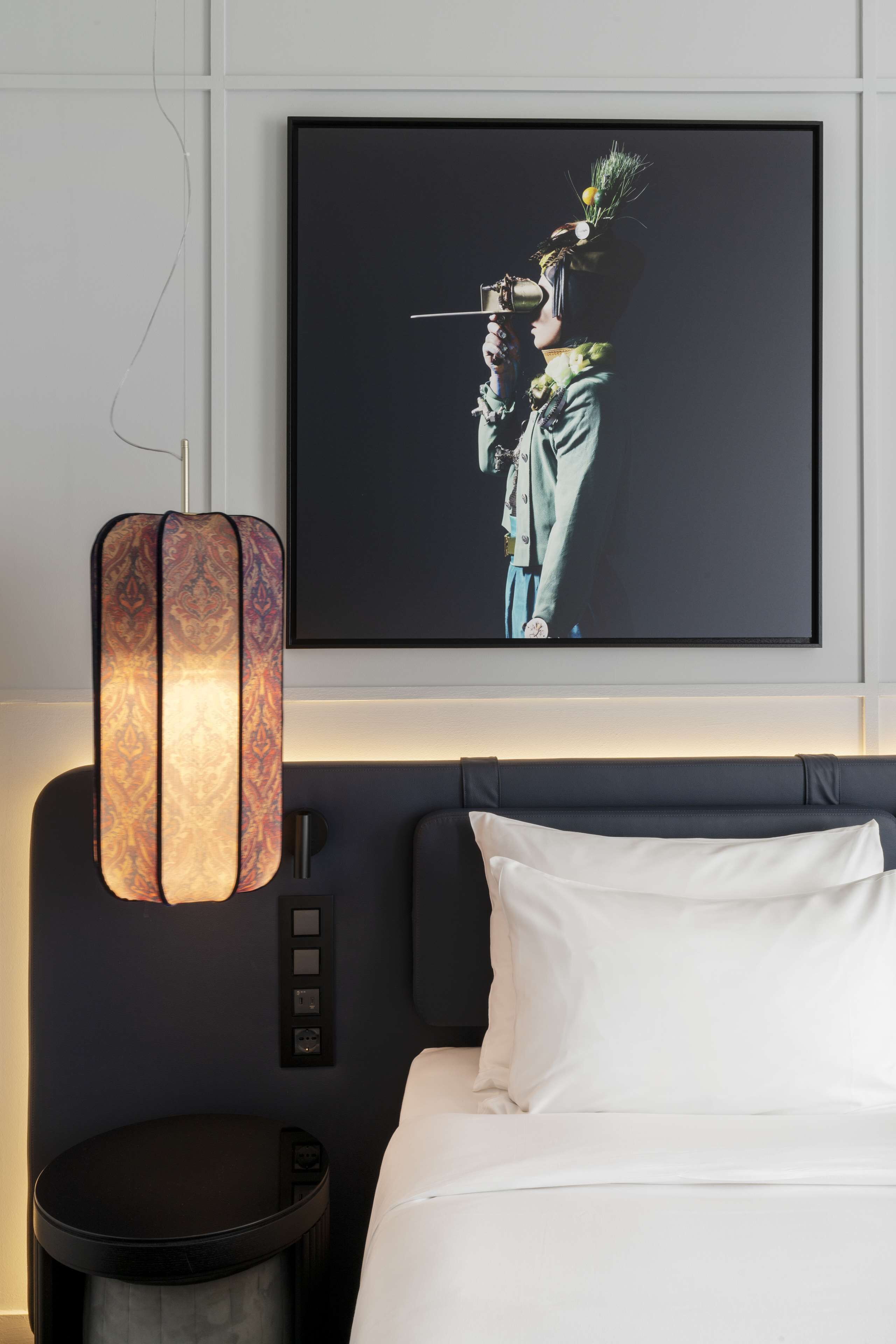 Een hotelkamer met een bed, een wandtelevisie en een decoratieve hanglamp.