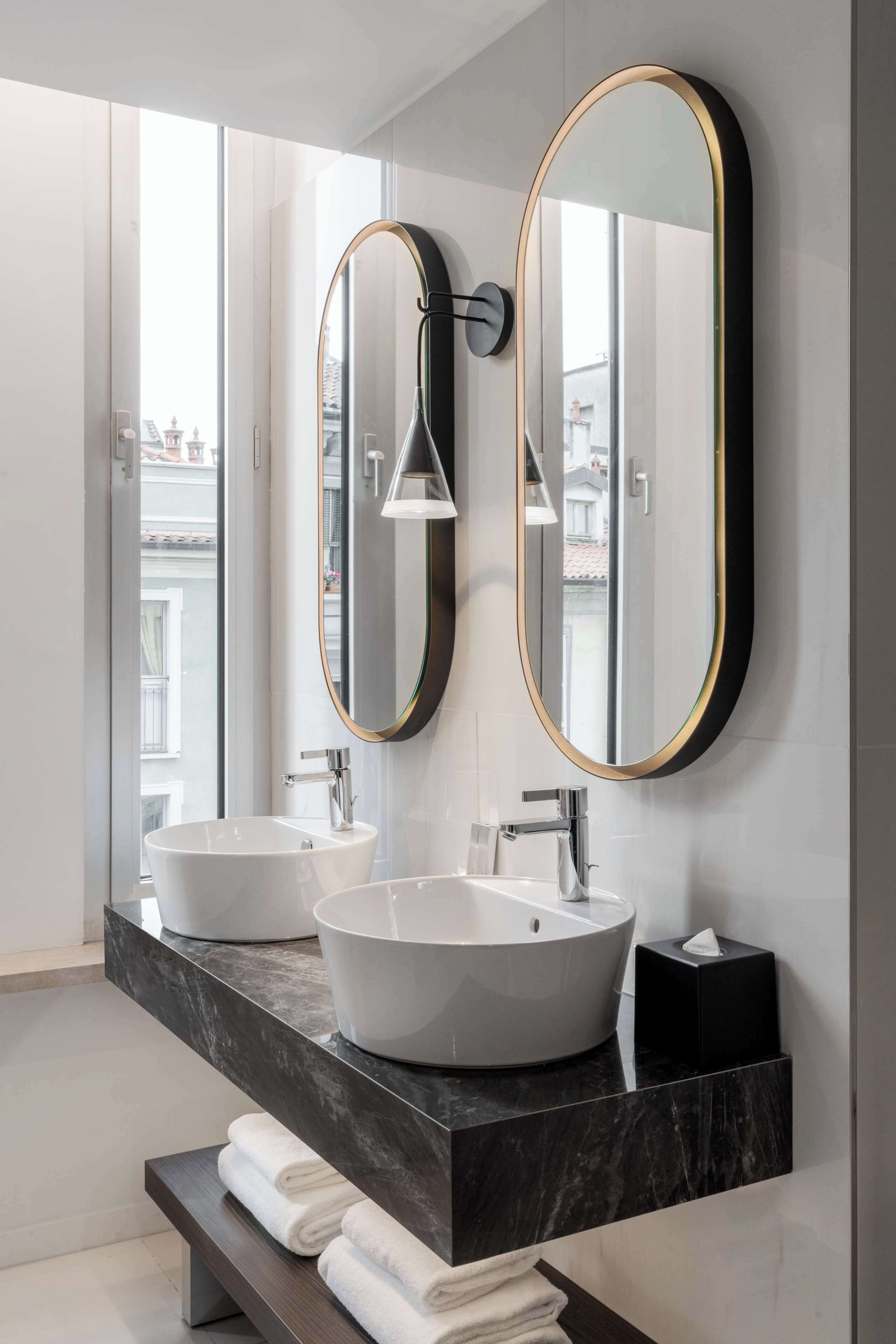 A modern bathroom with two sinks, a large mirror, and a bench with towels.