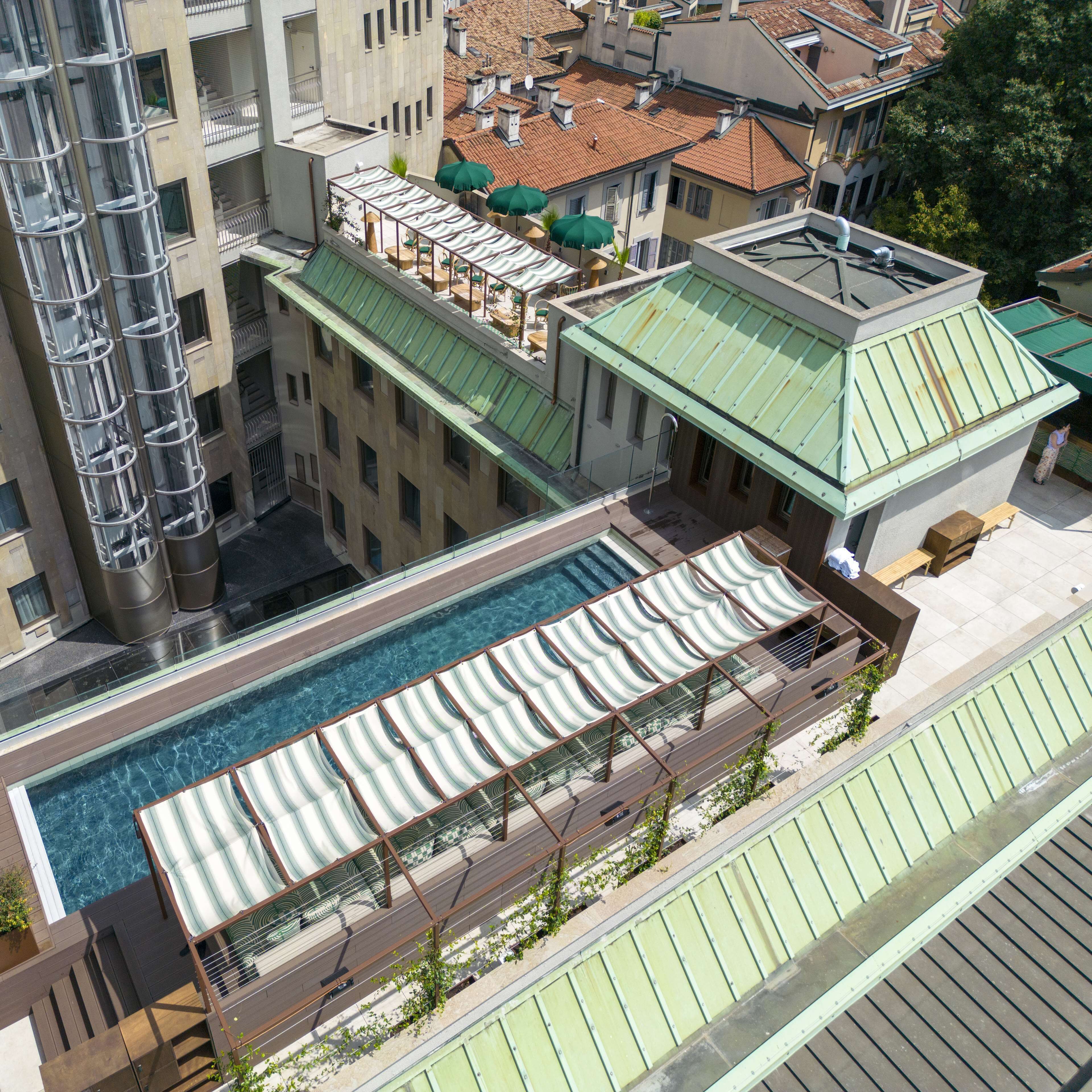 A rooftop pool with a green roof, surrounded by buildings with balconies and a large cylindrical structure.