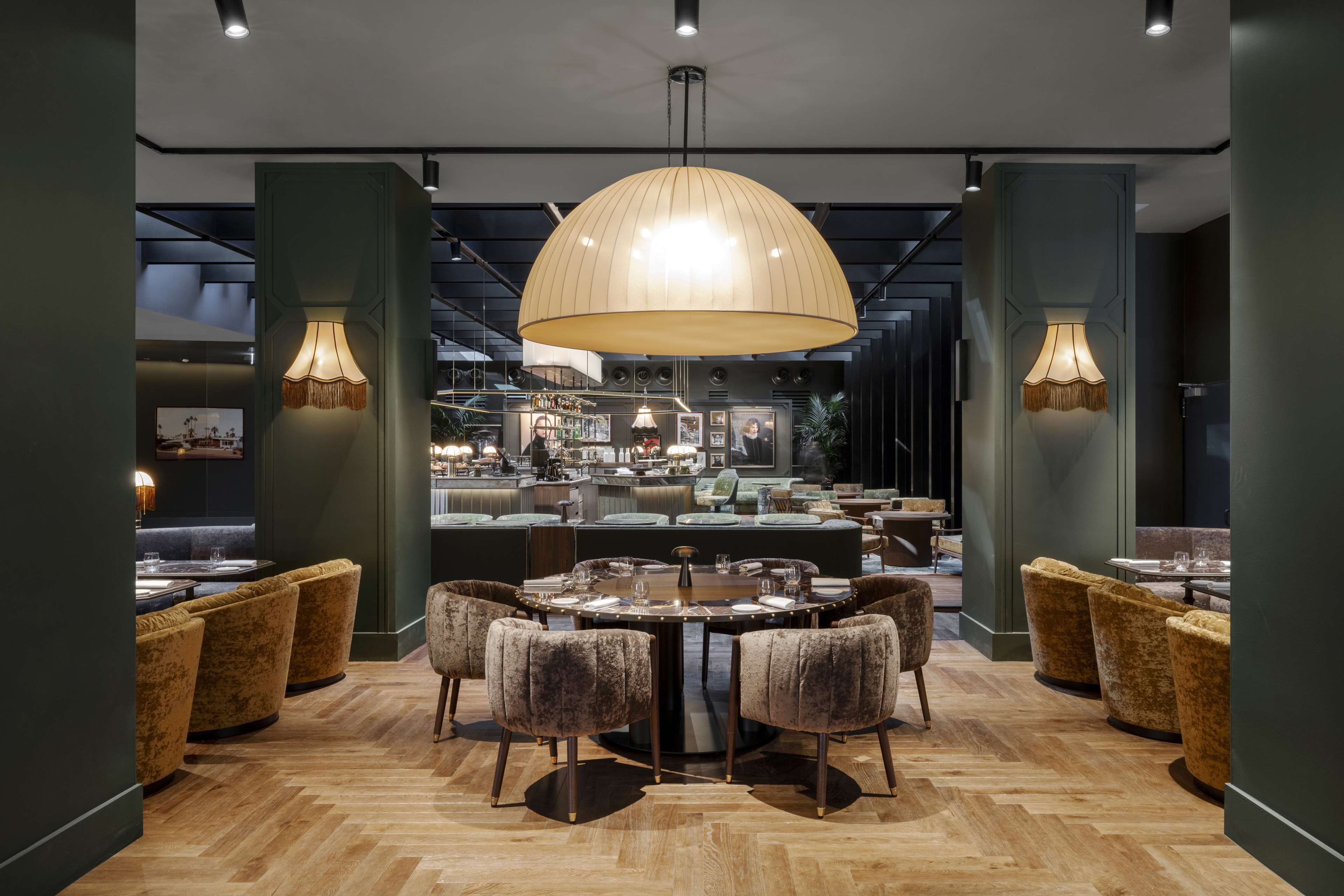 A modern restaurant with a central round table, cushioned seating, and pendant lighting.