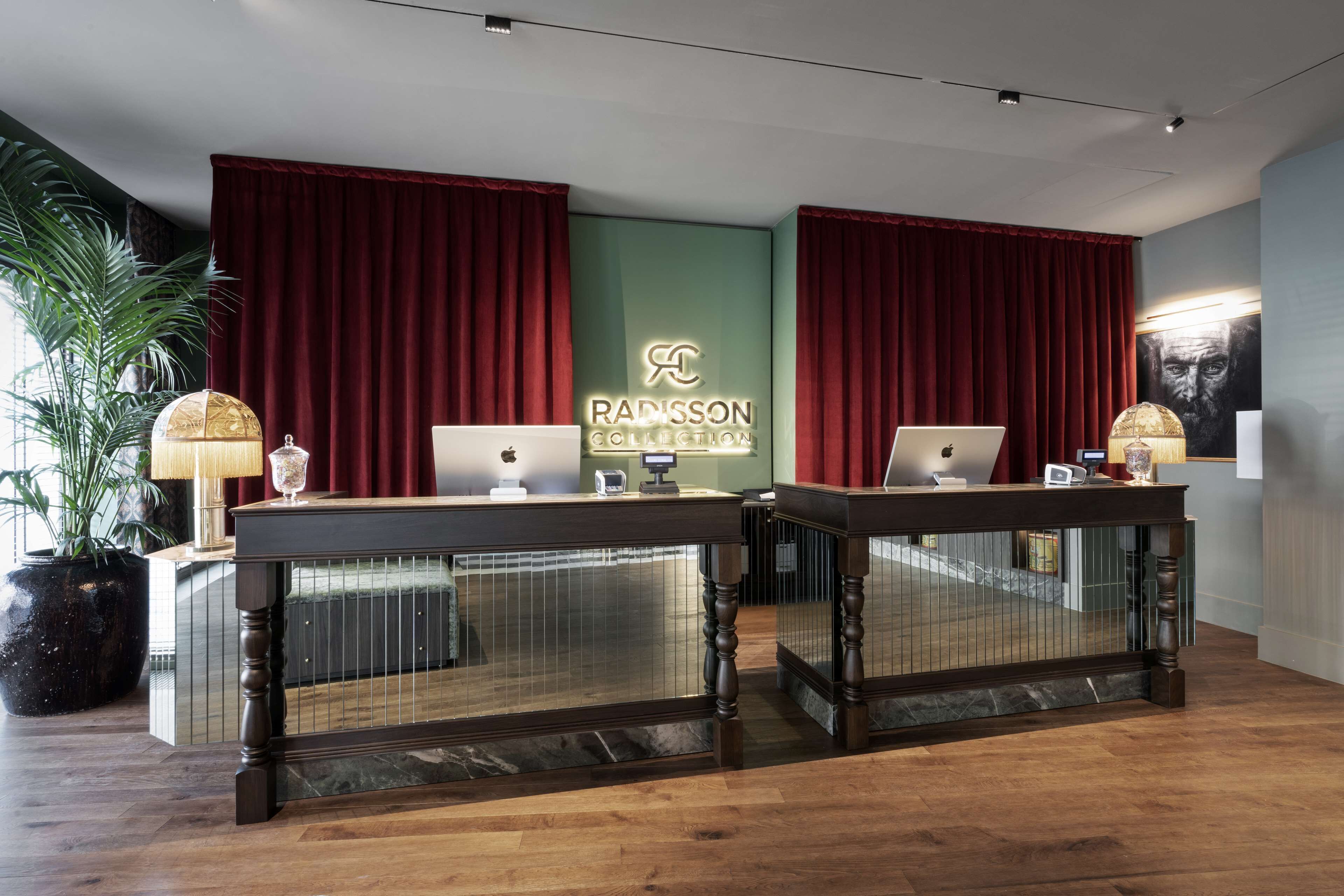 Zona de recepción con dos mostradores, cortinas rojas y una pared verde con el logotipo de Radisson Collection.