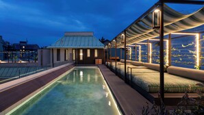 Un área de piscina en la azotea con cerramiento de vidrio, un lounge con asientos acolchados y vistas a la ciudad.