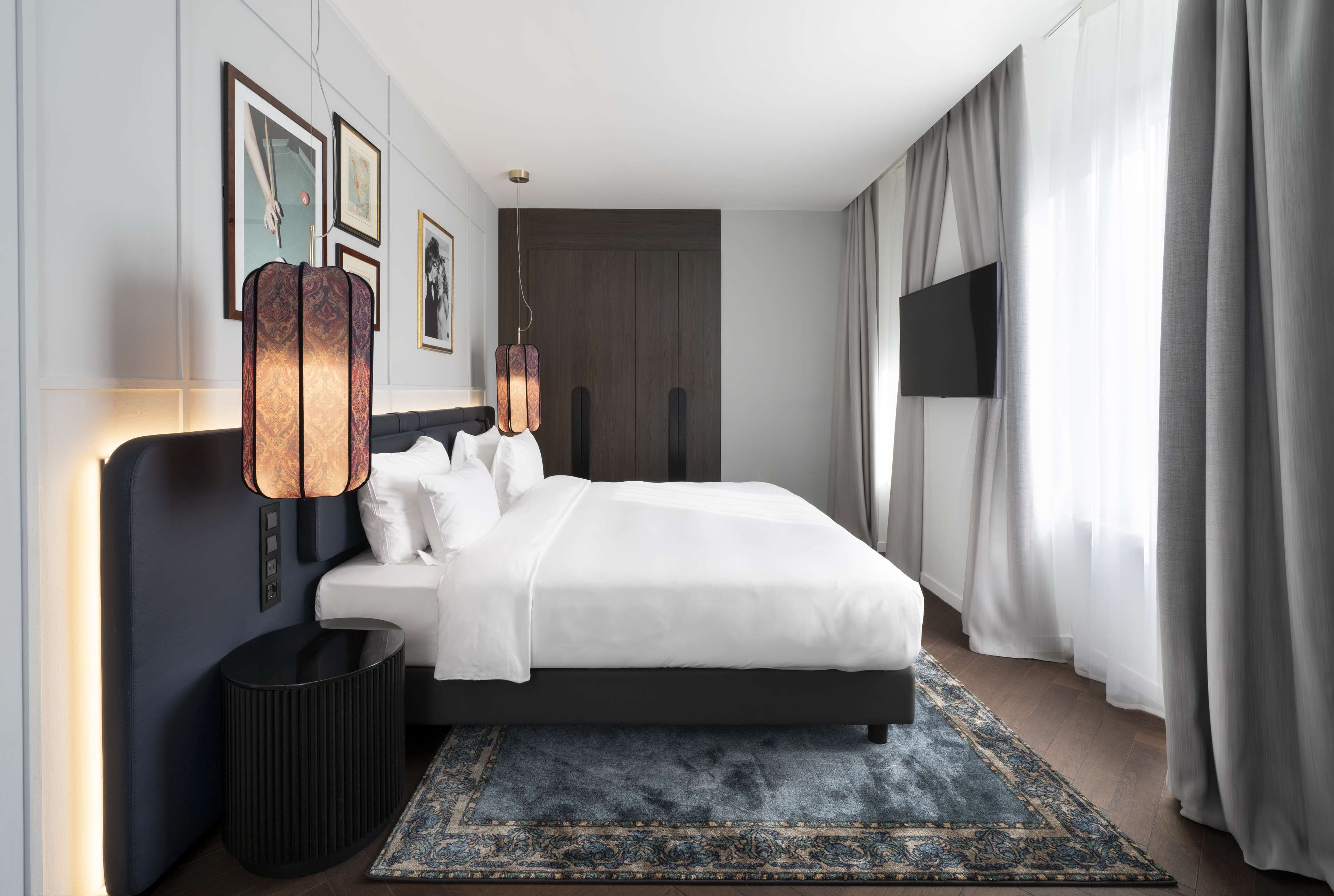 Una habitación de hotel moderna con una cama grande, un televisor de pantalla plana, una lámpara decorativa y una alfombra estampada.