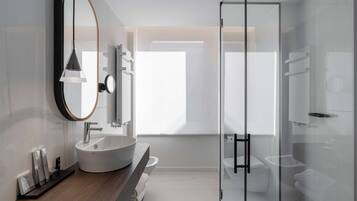 A modern bathroom with a large oval mirror, a white sink, and a glass-enclosed shower.
