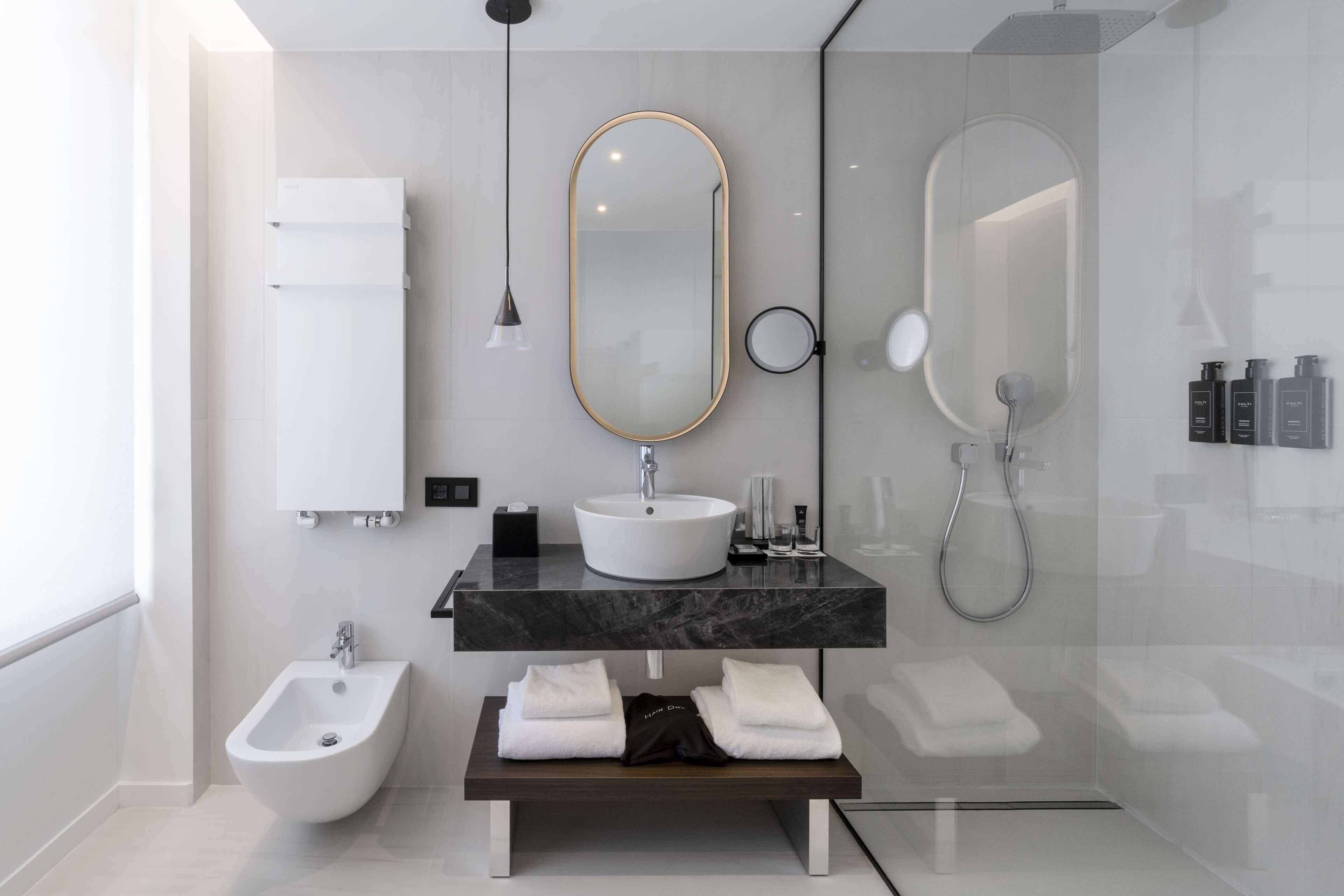 Un bagno moderno con bidet, lavandino con piano in marmo, ampio specchio e panca con asciugamani.