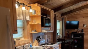 A wooden cabin kitchen with a granite countertop, stainless steel sink, white appliances, and a dining area with a TV.