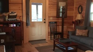 A cozy cabin interior with a wooden floor, a sofa, a dining table, and a television.