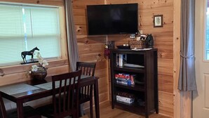 A wooden interior with a dining table, chairs, a TV mounted on the wall, and a bookshelf.