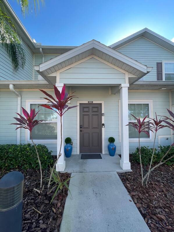 A two-story house with a front porch, a dark brown front door, and two potted plants on either side. - Cozy Townhome Near Disney Parks (Kissimmee)