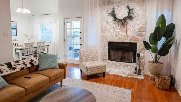 A living room with a stone fireplace, a sofa, a chair, and a large potted plant. - Ranch Glam Townhome with Indoor Fireplace (El Paso)