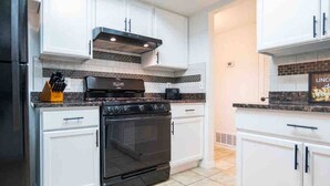 A modern kitchen with white cabinets, a black stove, and a tiled backsplash. - Ranch Glam Townhome with Indoor Fireplace (El Paso)