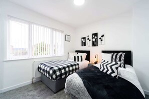 A bedroom with two beds, a radiator, a window with blinds, and wall art. - Nhyira 3 Bed Home w/Private Parking & Garden (Kingston upon Hull)