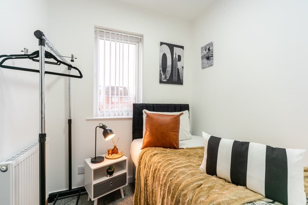A bedroom with a bed, a radiator, a window with blinds, a bedside table with a lamp, and a wall with a picture.