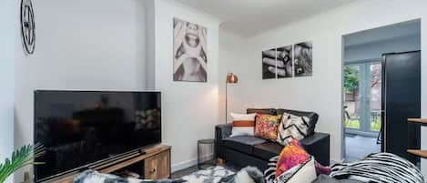 A modern living room with a flat-screen TV, a sofa with patterned cushions, and a decorative wall piece.
