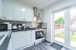 A modern kitchen with white cabinets, a built-in oven, and a large window. - Nhyira 3 Bed Home w/Private Parking & Garden (Kingston upon Hull)