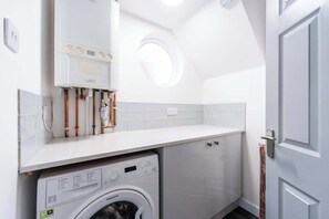 Une petite buanderie équipée d’un lave-linge, d’un chauffe-eau et d’un porte-serviettes.