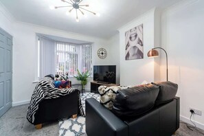 A modern living room with a sofa, a television, a lamp, and a clock on the wall. - Nhyira 3 Bed Home w/Private Parking & Garden (Kingston upon Hull)