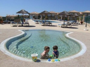 A swimming pool with a curved edge, surrounded by lounge chairs and umbrellas. - Boavista Golf Resort Apartment (Lagos)