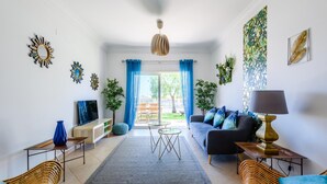 Una sala de estar moderna con un sofá, una mesa de centro y sillas, un televisor y vistas a un espacio exterior a través de una puerta de vidrio.