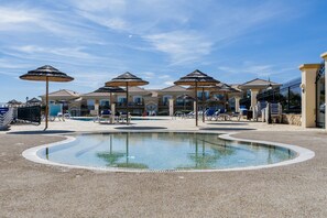 A pool area with lounge chairs and umbrellas, surrounded by a building with a tiled roof.
