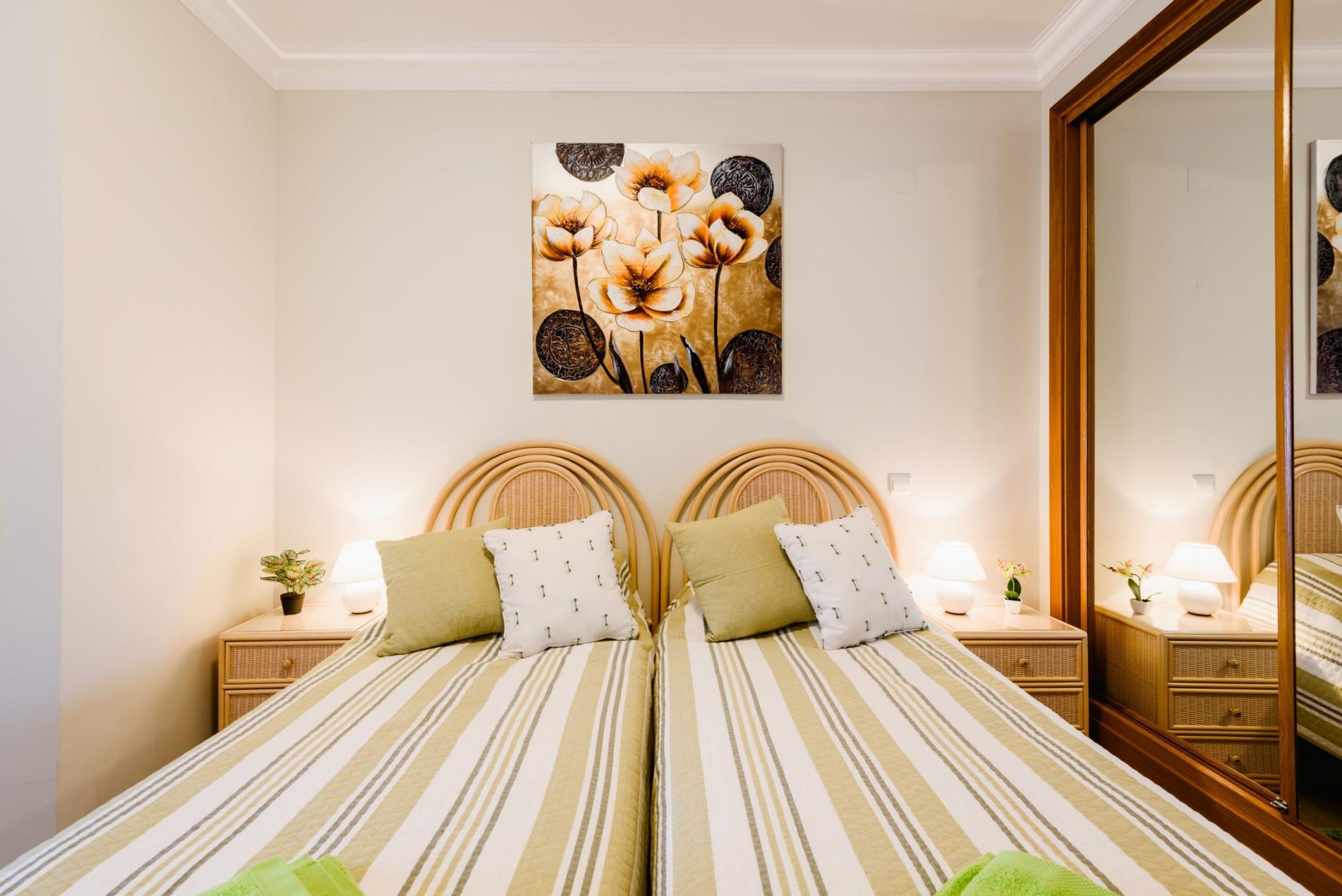 A double bed with striped bedding, two nightstands with lamps, a wall-mounted painting, and a mirror.