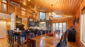 A spacious dining area with a long wooden table, multiple chairs, and a kitchen area with modern appliances.