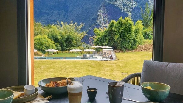 Una mesa de comedor con diversos platos y bebidas, con vistas a un paisaje montañoso a través de una ventana.