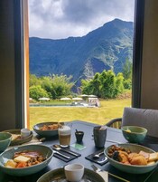 Una mesa de comedor con diversos platos y bebidas, con vistas a un paisaje montañoso a través de una ventana.