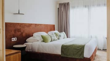A bedroom with a wooden headboard, a bed with white bedding and a green throw, a bedside table, and a hanging light fixture.