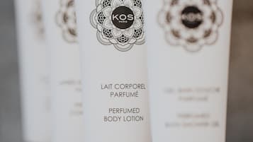A row of white lotion tubes with black caps, labeled "KOS PARIS" and "LAIT CORPOREL PARFUMÉ PERFUMED BODY LOTION".
