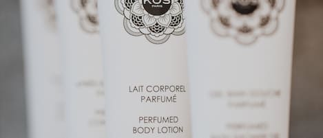 A row of white lotion tubes with black caps, labeled "KOS PARIS" and "LAIT CORPOREL PARFUMÉ PERFUMED BODY LOTION".