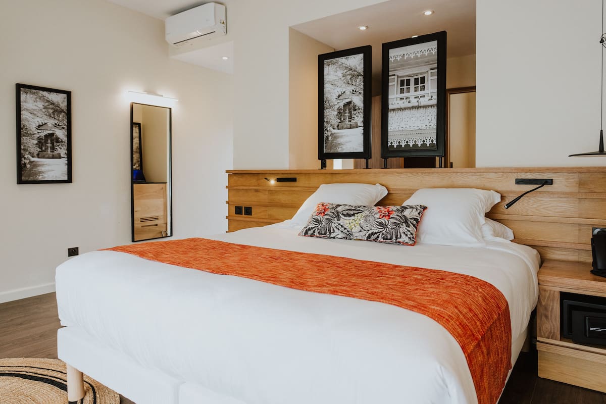 A hotel room with a large bed, a wooden headboard, a nightstand with a coffee maker, and two framed pictures on the wall.