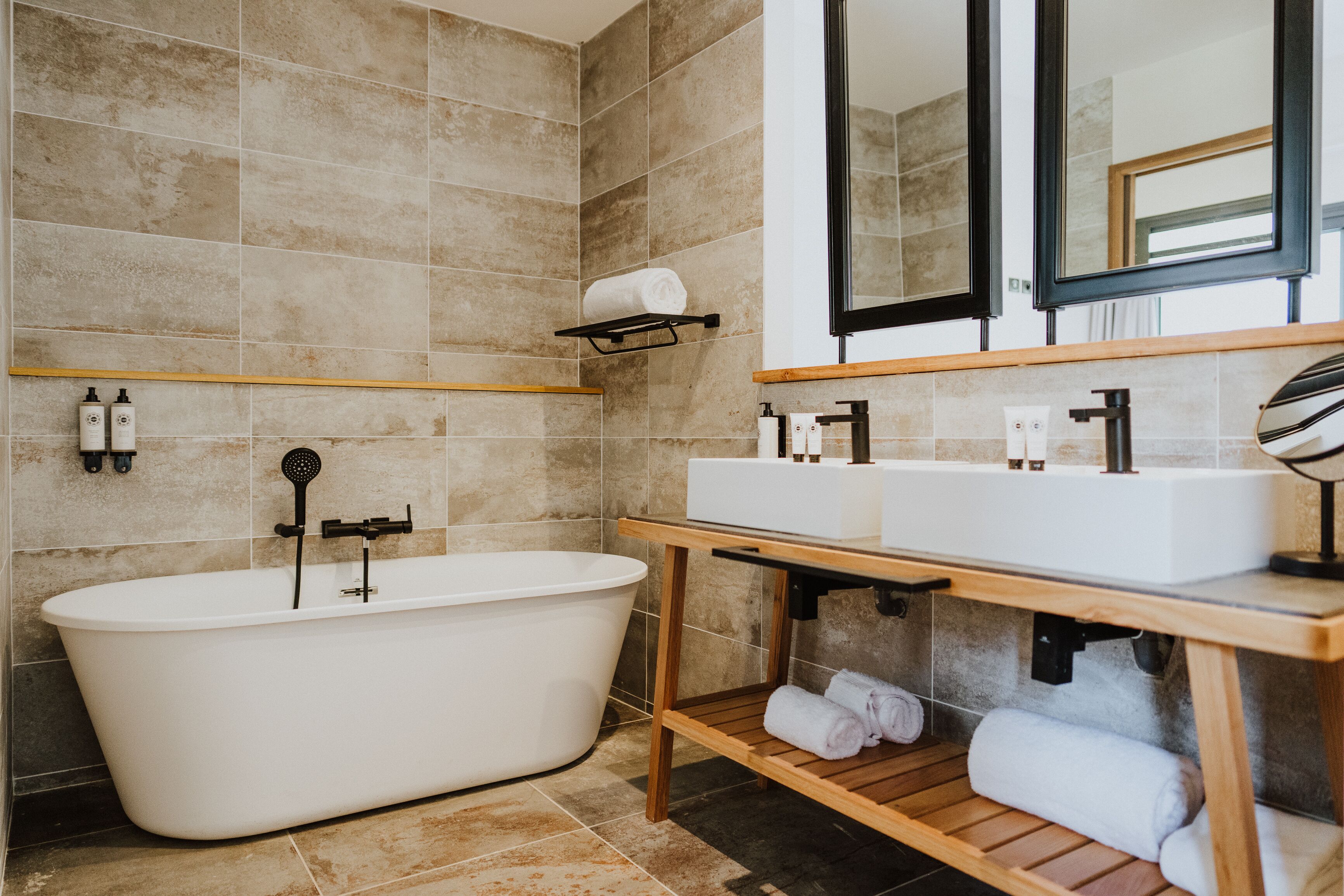 Un baño moderno con una bañera independiente, un tocador de madera con un lavabo y un espejo sobre el tocador.