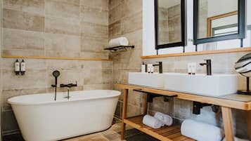 Un baño moderno con una bañera independiente, un tocador de madera con un lavabo y un espejo sobre el tocador.