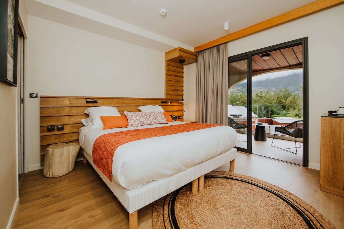 A modern bedroom with a large bed, wooden headboard, and a view of the outdoors through a sliding glass door.