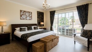 Un dormitorio con una cama grande, un candelabro, un balcón con cortinas y vistas a palmeras.