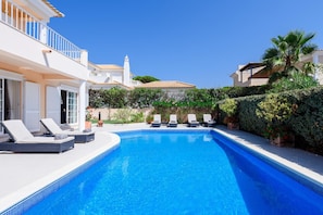 A swimming pool with lounge chairs, a white building with a balcony, and a palm tree. - Casa Lago - Varandas do Lago (Loulé)
