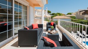 Un balcón con muebles de mimbre, una mesita y una piscina al fondo.