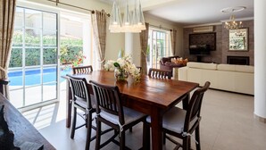 Un comedor con una mesa y sillas de madera, un jarrón de flores y vistas a una piscina a través de amplios ventanales.