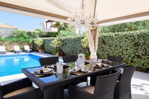 An outdoor dining area with wicker furniture, a pool, and a hedge backdrop. - Casa Lago - Varandas do Lago (Loulé)
