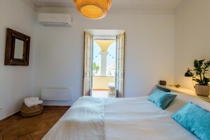 A bedroom with a large bed, a bedside table, a potted plant, and an open door leading to a balcony.