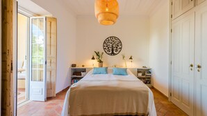 A bedroom with a large bed, a wall-mounted tree decoration, a bedside table with a lamp, and a door leading to an outdoor area. - Casa Omlandia With Pool - Lagos Old Town (Lagos)