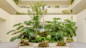 Ein mehrgeschossiges Atrium mit einem zentralen Gartenbereich, mehreren Etagen und einem gemusterten Boden.
