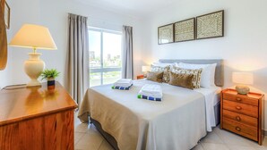 Ein Hotelzimmer mit einem großen Bett, einem Nachttisch aus Holz, einem Schreibtisch und einem Fenster mit Vorhängen.