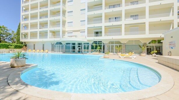 Ein modernes Hotel mit großem Schwimmbad, mehreren Balkonen und einem gepflegten Außenbereich.