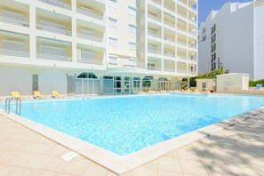 Una piscina con tumbonas y un edificio con varios balcones al fondo.