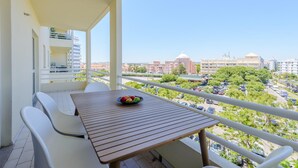 Ein Balkon mit Tisch und Stühlen, einer Obstschale und Blick auf die Stadtlandschaft.