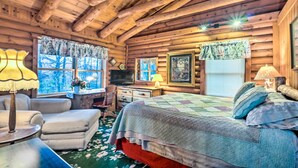 Ein Schlafzimmer in einer Blockhütte mit einem Bett, einem Schreibtisch, einem Sessel und einem Fernseher.